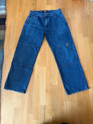 Vida Dickies Double Knee Jeans - Säljer ett par blå jeans från Dickies med rak passform och breda ben. Jeansen har klassisk femficksdesign, synliga sömmar över benen och är gjorda i slitstark denim. Perfekta för dig som gillar streetwear och avslappnad stil.