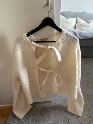 Krämvit stickad tröja med knytning - Trendig krämvit stickad tröja från Gina tricot med två knytband framtill och ribbstickad struktur. Tröjan har lång ärm och en avslappnad passform. Storlek xs men är stor i storlek så passar S. Aldrig använd