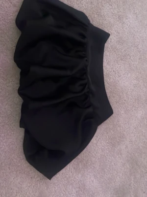 Svart puffig kortkjol i satin - Snygg svart kortkjol med puffig form och bred midja. Kjolen har en glansig satinliknande yta som ger en lyxig känsla och passar perfekt till trendiga outfits. Enkel att matcha med både toppar och boots.