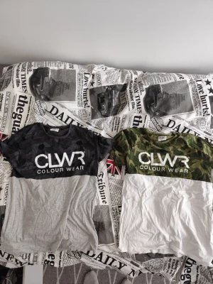 CLWR t-shirts med camo och logga - Två snygga t-shirts från CLWR med stor vit logga på bröstet. Ena t-shirten är svart/grå med mörkt camomönster upptill och grå nedtill, den andra är grön camo upptill och vit nedtill. Båda har rund hals och är i mjukt bomullsmaterial.