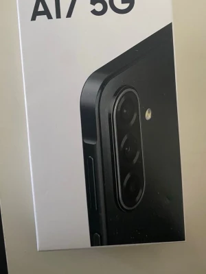 Samsung Galaxy A17 5G mobiltelefon - Samsung Galaxy A17 5G är en modern smartphone med stilren svart design och rundade kanter. Telefonen har en trippelkamera på baksidan och LED-blixt. Lådan är vit med tydlig Samsung-logga och produktnamn. Perfekt för dig som vill ha snabb 5G och snygg look. Helt ny dock är paketet öppet men telefonen är helt ny pappret på telefonen är inte öppet 