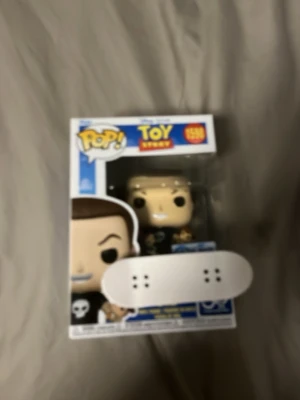 Funko Pop Toy Story och fingerboard - Säljer en Funko Pop-figur från Toy Story i originalförpackning samt en vit fingerboard med färgglad text och svarta hjul. Perfekt för samlare eller dig som gillar coola prydnader och små skateboards.