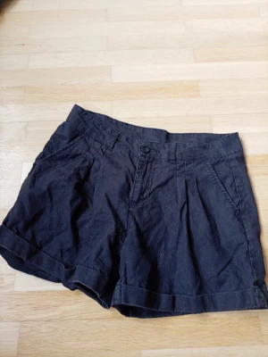 Svarta shorts från Vila i linne - Svarta shorts från Vila i mjukt linnematerial. De har hög midja, uppvikta benslut och sidfickor. Perfekta för varma dagar och enkla att matcha med olika toppar.