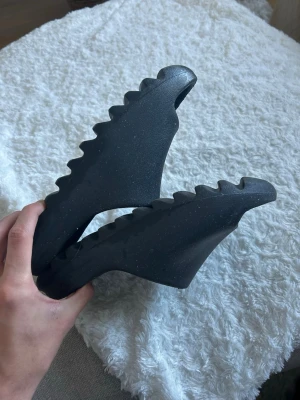 Svarta Adidas tofflor Yeezy Slide - Säljer ett par svarta Adidas Yeezy Slide med chunky, sågtandad sula. Tofflorna är gjorda i ett mjukt och flexibelt gummimaterial och har en stilren, minimalistisk design med Adidas-logga i fotbädden.
