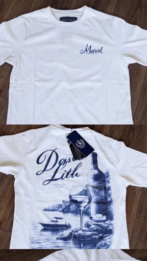 Vit t-shirt Leon Marcel med tryck - Vit t-shirt från Leon Marcel med blått tryck på bröstet och stort motiv på ryggen med vinflaska, glas och havsmiljö. Rund hals och korta ärmar. Perfekt för dig som gillar stilrena plagg med coola detaljer.