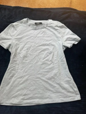 Ljusblå t-shirt - En enkel vit t-shirt från BikBok i storlek S med rund hals och korta ärmar. Tillverkad i mjuk bomull för en skön känsla och klassisk passform. Perfekt att matcha med jeans eller shorts för en clean look. Den är figurnära och jätte mjuk