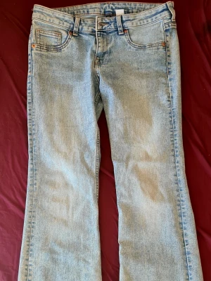 Ljusblå bootcut jeans - Säljer ett par ljusblå bootcut jeans i klassisk denim med råa kanter nertill. Jeansen har en utsvängd passform från knät och ner, vilket ger en retro och avslappnad vibe. Perfekta för dig som gillar vintageinspirerad stil och vill ha ett par bekväma jeans med mycket attityd.