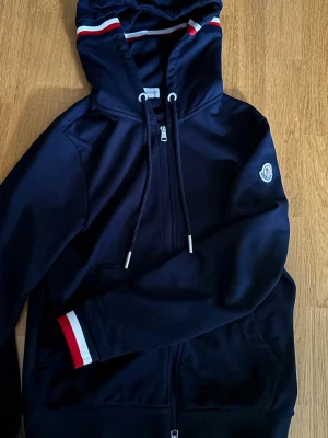 Moncler zip hoodie navy blå - Snygg mörkblå/navy zip hoodie från Moncler, luva med vita och röda detaljer. Storlek S men skulle säga att den passar XS också.