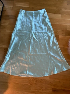 Ljusblå satinkjol i lång modell - Snygg ljusblå långkjol i satin med lätt glansig finish. Kjolen har en enkel och stilren design med lätt utsvängd form. Perfekt för dig som gillar en elegant och trendig look.