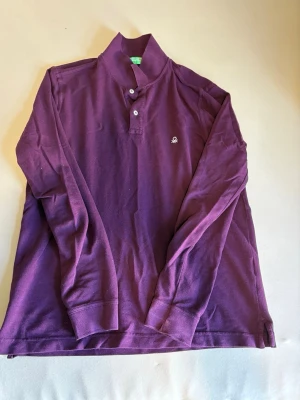 Lila långärmad skjorta Benetton - Långärmad lila skjorta från Benetton med klassisk krage och knappar framtill. Skjortan har en liten broderad logga på bröstet och är tillverkad i mjuk bomull. Perfekt för en avslappnad men stilren look.