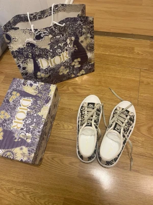 Dior Oblique låga sneakers - Säljer ett par Dior Oblique sneakers i tyg med beige och svart mönster, vita gummisulor och beige snörning. Klassisk Dior-logga på sidan och tungan. Snygg och trendig modell som passar perfekt till streetwear.