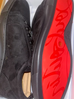 Svarta Louboutin sneakers i mocka- svarta loubs - Snygga svarta sneakers från Christian Louboutin i mjuk mocka med klassisk röd sula och svarta skosnören. Låg modell med diskreta detaljer och exklusiv känsla. Perfekta för dig som vill ha något stilrent men ändå sticker ut. Passar vardagligt men även lite finare med kostym. Använt 3 gånger. 