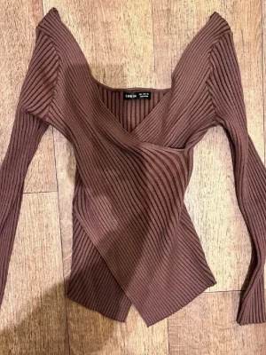 Brun omlottopp från SHEIN - Trendig brun omlottopp från SHEIN med ribbad struktur och v-ringad hals. Långärmad modell i stretchigt material som sitter snyggt och markerar midjan. Perfekt för dig som gillar en modern och stilren look.