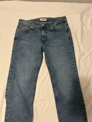 Blå raka jeans från Jack & Jones - Snygga blå jeans från Jack & Jones med klassisk femficksmodell och raka ben. Jeansen har normal midja, bälteshällor och stängs med dragkedja och knapp. Perfekta till en avslappnad stil och tillverkade i mjukt denimtyg.