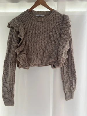 Beige stickad från NA-KD - Supersöt beige stickad tröja från NA-KD med volangdetaljer längs ärmar och framsida. Den är gjord i ett grovt stickat material. Perfekt för kalla sommarkvällar eller vintern ❤️ själv älskar jag den men går inge till användning. ( inget fel på den) kolla bild 3 för att se ljuset på den😇