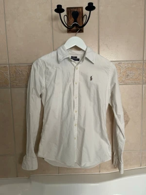Ralph Lauren skjorta - Jätte snygg vit ralph lauren skjorta. Skjortan är slim fit. Knappt andvänd och passar till princip varje outfit. Jätte snygg nu inför sommarn, släpps för ett schysst pris vid snabb affär. 