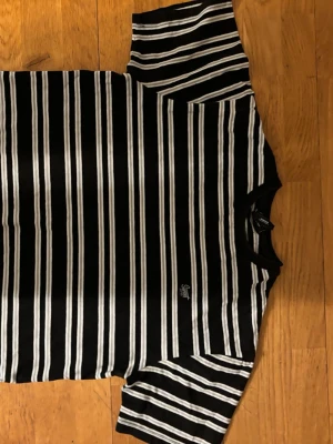 Svartvit randig t-shirt från Sweet SKTBS - Snygg svart t-shirt från Sweet SKTBS med vita horisontella ränder och diskret logga på bröstet. Klassisk rund halsringning och korta ärmar. Perfekt till jeans eller shorts för en clean och enkel stil.