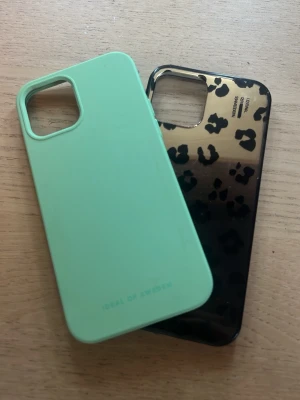 Två mobilskal från IDEAL OF SWEDEN (iPhone 12) - Säljer två snygga mobilskal från IDEAL OF SWEDEN. Ett är mintgrönt i matt silikon och det andra är glansigt svart med leopardmönster. Båda har öppning för kamera och passar perfekt för dig som vill ha stilrena och trendiga skal till mobilen.