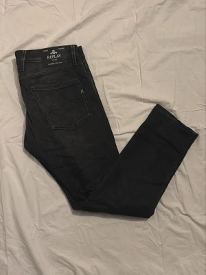 Replay - Ett par svarta replay jeans, i storleken 33W 32L. Jeansen har ett skönt material och är i modelen anbass. Hör av er vid minsta fråga. A=44cm B=76cm C=26cm D=18cm E=16cm