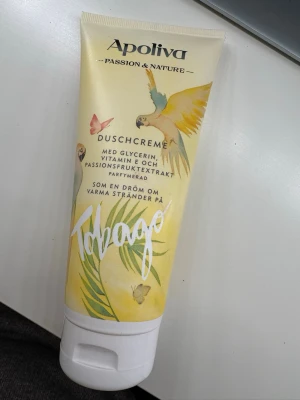 Apoliva Tobago duschcreme - Fräsch duschcreme från Apoliva med doft av passion och nature. Innehåller glycerin, vitamin E och passionsfruktextrakt. Tuben har ett tropiskt motiv med papegoja och fjärilar i mjuka gula och gröna toner. Produkten är helt ny i förpackning, ej testad. 