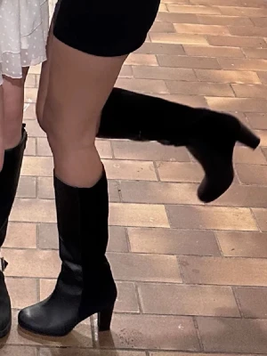 Svarta höga stövlar med klack - Snygga svarta stövlar med hög klack och rundad tå. Stövlarna är i en mix av slätt skinn och mocka, vilket ger en cool kontrast. Perfekta till höstens outfits och funkar lika bra till jeans som till kjol.