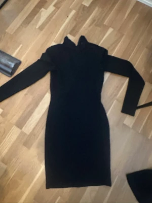 Svart långärmad klänning - Säljer en svart, långärmad klänning med figurnära passform och hög krage. Klänningen har en dragkedja i ryggen som ger en snygg detalj. 