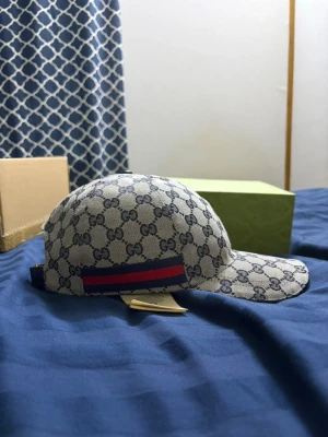 Gucci keps med GG-mönster - Snygg keps från Gucci i beige och blått med klassiskt GG-monogram över hela kepsen. Kepsen har en böjd skärm och en röd-blå rand på sidan. Tillverkad i canvasmaterial som ger en exklusiv känsla.