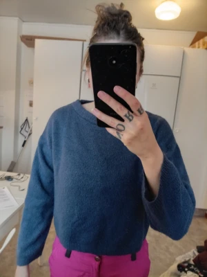 Mörkblå croppad stickad tröja - Mysig mörkblå stickad tröja med croppad passform och rund halsringning. Tröjan har långa ärmar och en enkel, stilren design som passar perfekt till jeans eller kjol. Perfekt för lager-på-lager under kyliga dagar.