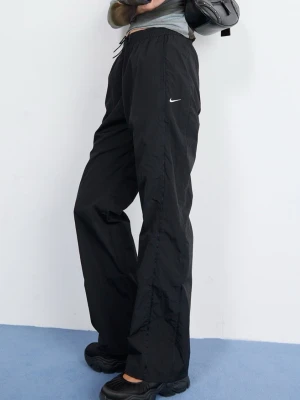 Svarta vindbyxor från Nike - Säljer ett par svarta mjukisbyxor från Nike med avslappnad passform och resår i midjan med dragsko. Byxorna har en liten vit Nike-logga på benet och är tillverkade i ett lätt, sportigt material. Perfekta för en chill och sportig look.