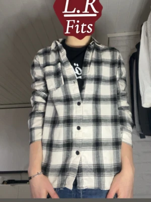 Svartvit rutig skjorta - Säljer en svartvit rutig skjorta med klassisk krage och knäppning framtill. Skjortan har en bröstficka och är tillverkad i ett mjukt bomullstyg. Perfekt för en avslappnad och trendig look.