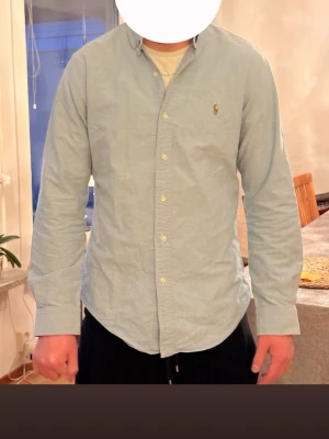 Ljusblå skjorta från Ralph Lauren - Klassisk ljusblå skjorta från Ralph Lauren med button-down krage och broderad logga på bröstet. Skjortan har långa ärmar och knäppning framtill. Perfekt för en stilren och avslappnad look. M men passar som s också