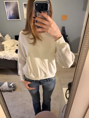 Vit sweatshirt med rund hals - En enkel och stilren vit sweatshirt med rund hals och långa ärmar. Tröjan har en avslappnad passform och ribbade muddar vid ärmslut och nederkant. Perfekt för en casual look och lätt att matcha med jeans eller andra byxor.