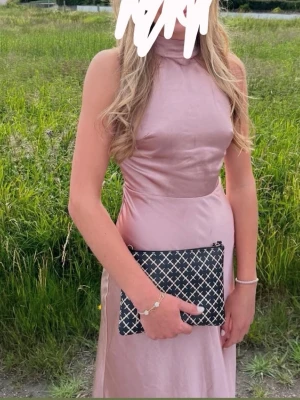 Balklänning  - Elegant rosa långklänning med öppen rygg och knytband i nacken. Klänningen har en slät design och är perfekt för festliga tillfällen. Den är ärmlös och har en vacker glansig yta som ger en lyxig känsla. Nypris 1799kr passar både xs och s