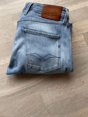 Replay anbass - Säljer ett par ljusblå jeans från Replay med raka ben och slitningar på låren och knäna. Jeansen har klassisk femficksdesign, läderpatch bak i midjan och är gjorda i mjuk denim. Perfekta för en avslappnad och trendig look. Storlek 32/32