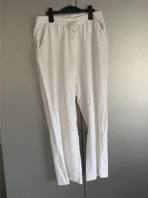 Vita linnebyxor med resårmidja - Snygga och luftiga vita linnebyxor med resår i midjan och raka ben. Byxorna har sidfickor fram och en bakficka. Perfekta för en avslappnad och stilren look under varma dagar.