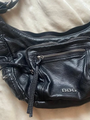 Cool väska - Massaaaaaa fickor: fyra små på sidorna, en stor ytterficka på framsidan och en liten utanpå den och en innerficka inuti själva väskan. Axelbandet är väldigt justerbart. På bilderna är den så kort som det går att göra den.