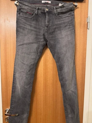 Grå slim fit jeans Tommy Jeans - Snygga grå slim fit jeans från Tommy Jeans med klassisk femficksmodell och diskreta slitningar. Jeansen har en rak passform och röda sömdetaljer vid fickan. Tillverkade i mjukt denimtyg som ger en bekväm känsla och cool look.