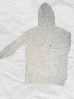 Ljusgrå merinoull hoddie - En stilren ljusgrå hoodie med huva och snören. Tillverkad i mjukt material som är otroligt skön. Perfekt för en avslappnad look och enkel att matcha med jeans eller joggers. Klassisk passform och ribbade muddar vid ärmslut och nederkant. Rätt så lågt pris eftersom att det är en defekt vid kragen men bortsett från det är det en sjukt stilren hoddie enligt mig