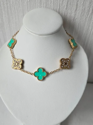 Blomma/klöver armband, rostfritt stål,  18k guldpläterad  - Snyggt armband med guldfärgad kedja och klöverformade detaljer. Vissa klöver är turkosa och andra är dekorerade med små stenar. Justerbar storlek 