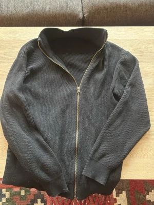 Svart ribbad zip cardigan - Säljer en svart ribbad tröja med dragkedja framtill och hög krage. Storlek XS men passar S. Den är lite nopprig här och där.