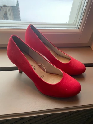 Röda pumps i mockaimitation - Snygga röda pumps med rund tå och mellanhög klack. Skorna är i mockaimitation och har en klassisk, stilren design som passar till många olika outfits. Perfekta för dig som vill sticka ut med färg på fötterna. Köpta på sellpy för 100kr