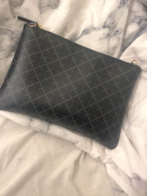 Svart axelväska med rutmönster - Snygg svart axelväska med diskret rutmönster och guldfärgade detaljer. Väskan har avtagbar och justerbar axelrem samt dragkedja upptill. Tillverkad i ett tåligt konstläder som ger en stilren look.