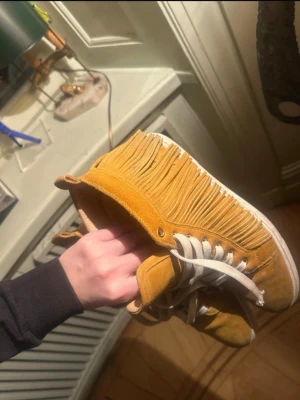 Gula mockasneakers med fransar - Unika Christian Louboutin sneakers i  mocka med coola fransdetaljer längs sidorna och vita snören. Perfekta för dig som vill sticka ut med din stil. Fransarna ger en boho-vibe. 