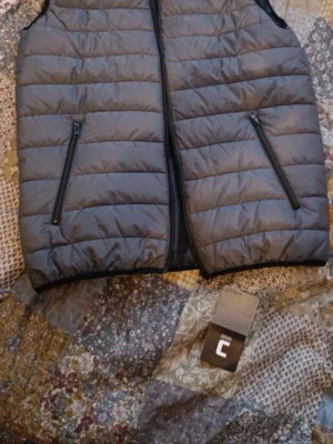 Grå dunväst från Cellbes - Helt ny Snygg grå dunväst från Cellbes med quiltad design och två dragkedjeförsedda fickor framtill. Västen har en rak passform och stängs med dragkedja. Perfekt för lager på lager och enkel att matcha med olika outfits.