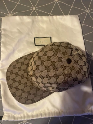 Gucci keps med monogrammönster - Snygg Äkta keps från Gucci i beige och brunt med klassiskt GG-monogram över hela kepsen. Kepsen har böjd skärm och är tillverkad i canvasmaterial. Perfekt för dig som vill sticka ut med en lyxig accessoar. Köpt 2024 sommaren för 2700 jag säljer nu den för 2100 den är i väldigt bra skick använt fåtal gånger säljer den pågrund av ändrad stil använder inte den längre . Har dustbag kvar men ej boxen tyvärr hör av dig om du är intresserad . Den billigaste du kan hitta på appen först till kvarn  