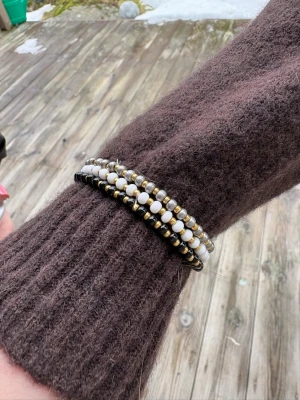 Set med tre pärlarmband - Säljer ett set med tre armband gjorda av små pärlor i vitt, guld och svart. Armbanden är elastiska och kan bäras tillsammans eller separat för en snygg layering-effekt. Perfekt accessoar för att lyfta din outfit med lite extra bling.