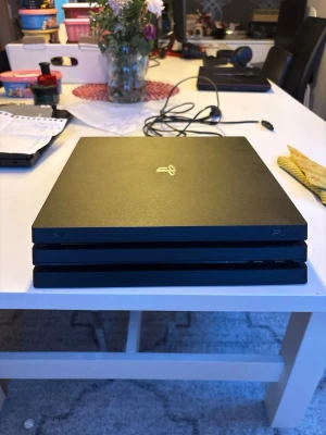 PlayStation 4 Pro svart konsol - Säljer en svart PlayStation 4 Pro från Sony. Konsolen har en stilren, fyrkantig design med tre lager och PlayStation-loggan i silver på ovansidan. Tillverkad i matt plast och passar perfekt för gaming och underhållning.