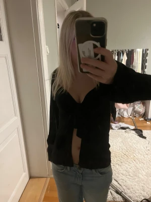 Svart omlottopp med knyt - Snygg svart omlottopp med knyt framtill och djup v-ringning. Toppen är croppad och har långa ärmar, perfekt för att lyfta vilken outfit som helst. Passar dig som gillar trendiga och stilrena plagg.