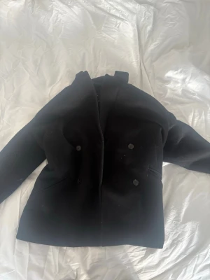 Svart oversized kavaj med dubbelknäppning - Snygg svart oversized kavaj med dubbelknäppning och breda slag. Klassisk modell med två framfickor och rak passform. Perfekt att styla till både jeans och kostymbyxor för en trendig look.