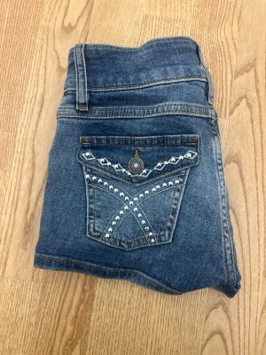 Blå jeansshorts med broderade detaljer - Snygga blå lågmidjade jeansshorts från Subdued köpta i italien med broderade detaljer och nitar på bakfickorna. Vädligt bra passform.